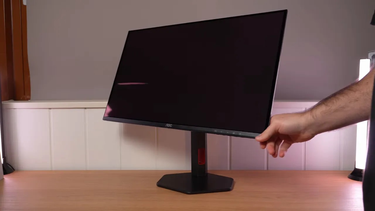 AOC Q27G4ZDR sobre escritorio con peana y mano ajustando la inclinación