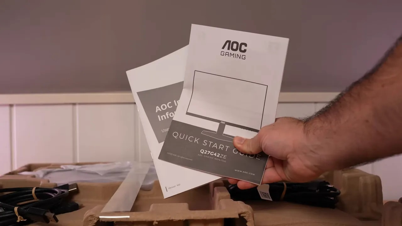 Mano mostrando un cable incluido en la caja del monitor AOC Q27G4ZE