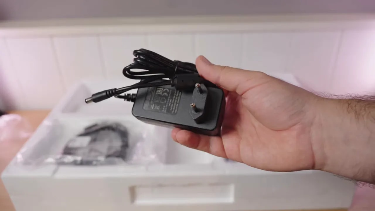 Fuente de alimentación y cables del monitor KTC H27T27 en la mano durante la revisión de accesorios