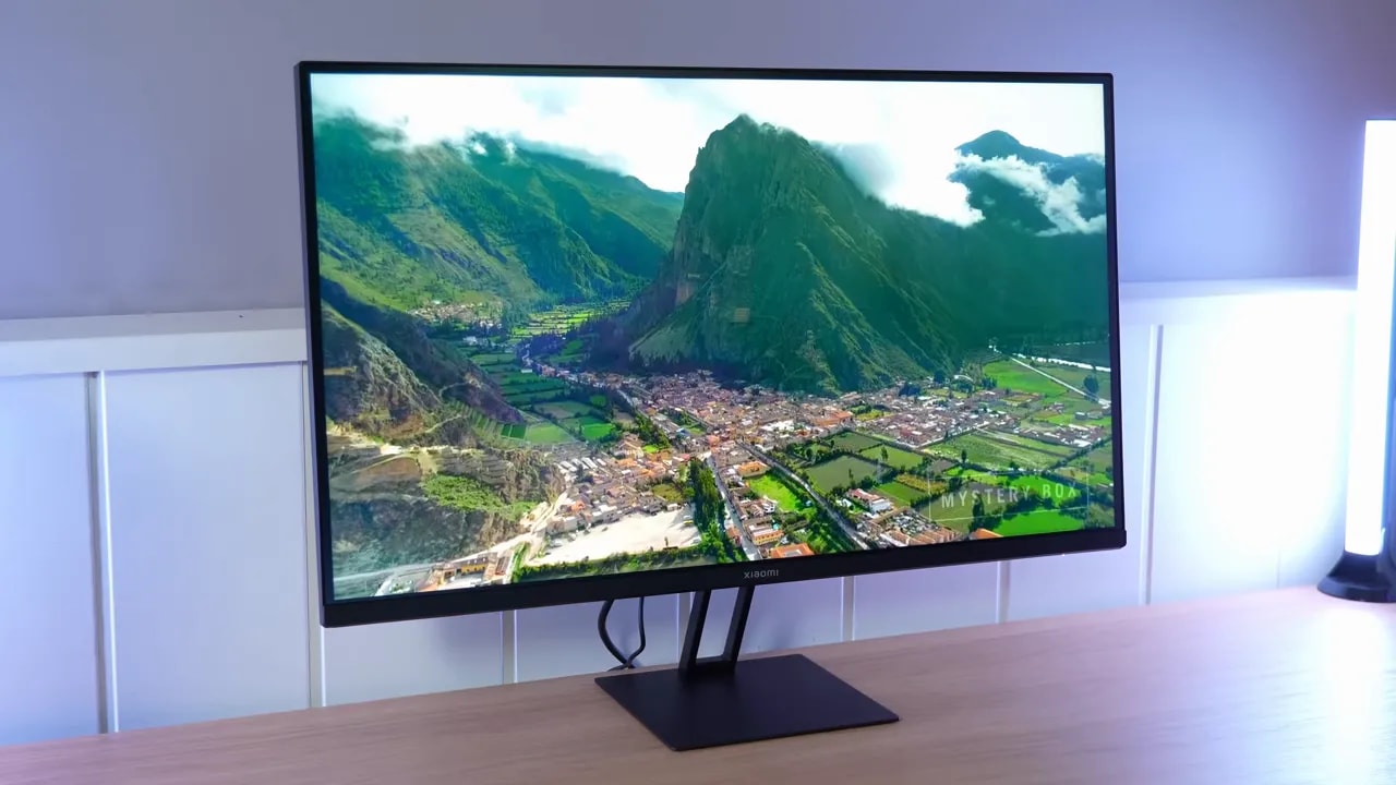 Monitor Xiaomi G27Qi mostrando una vista de montaña y ciudad en una pantalla de escritorio